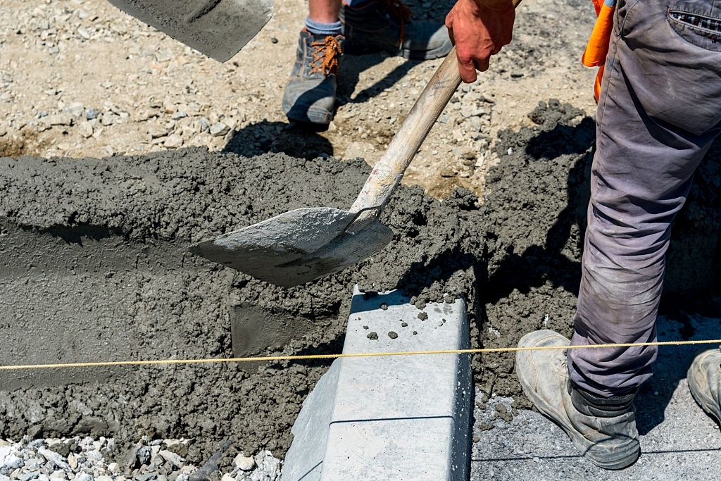Рабочий укладывает тощий бетон М300 В22,5 лопатой